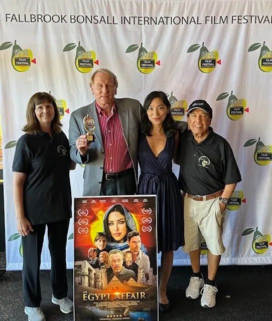 An award winner on the step-and-repeat with the poster for “An Egypt Affair”.